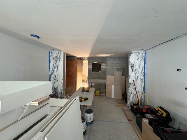 Narrow unfinished hallway with stacked drywall, tools, and construction materials under renovation