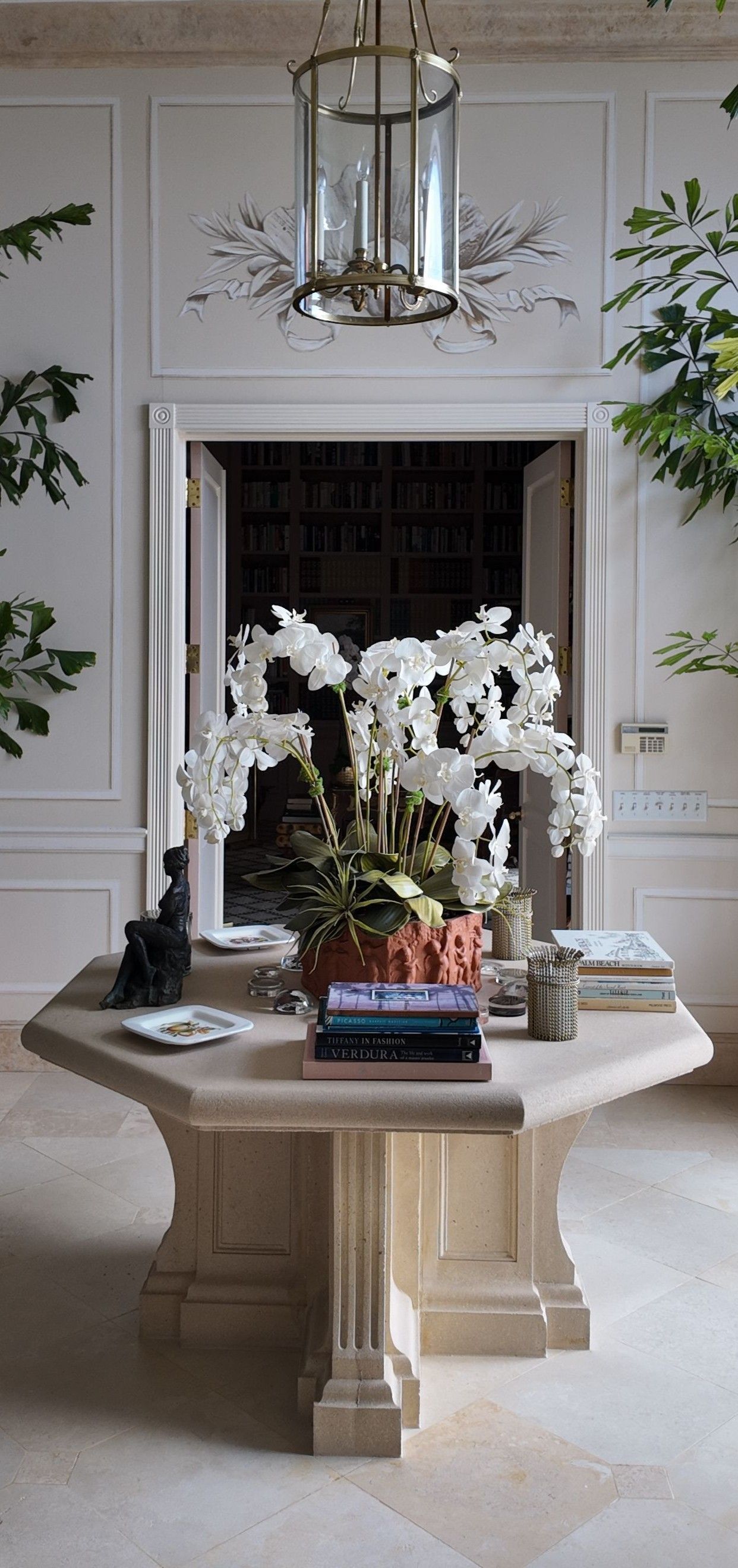 Elegant living room with a stone table, white orchids, and a dark fireplace under a chandelier.