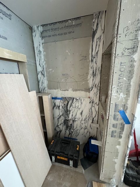 Partially finished interior wall with construction materials, tools, and wood panels in a narrow room
