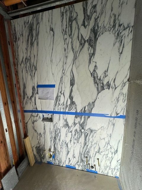 Marble-look wall panel with blue tape markers in an unfinished bathroom area