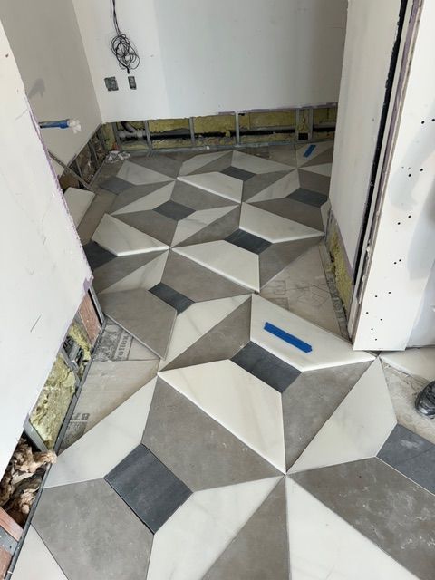Patterned tile floor in a doorway under construction, with blue tape on the floor and exposed wall edges