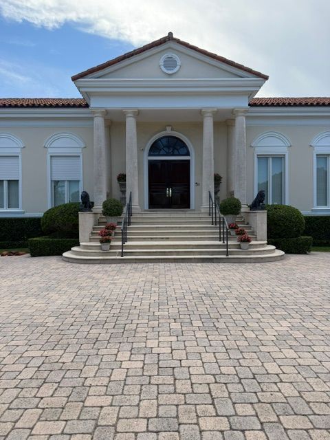 White building with columns and steps, viewed from a paved courtyard under a blue sky