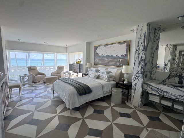 Bright bedroom with large windows, geometric rug, bed, armchair, and marble fireplace accents