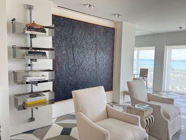 Modern living room with white chairs, a large dark wall panel, and a bookshelf with books and decor.