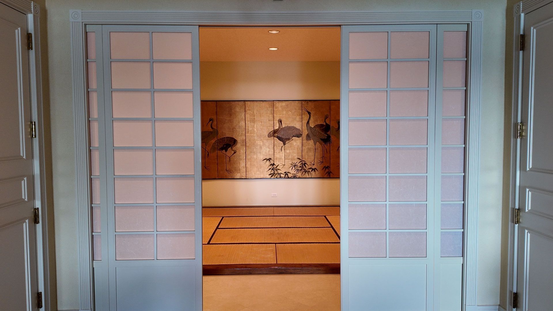 Open double doors into a tatami room with a painted mural and warm lighting