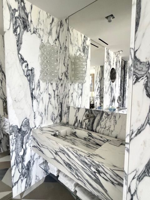 Marble-patterned bathroom with sink, mirror, and shower walls in black, white, and gray.