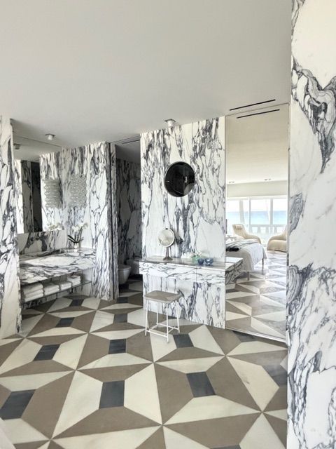 Marble-themed bathroom with geometric tile floor, vanity, and round mirror, in black, white, and gray.