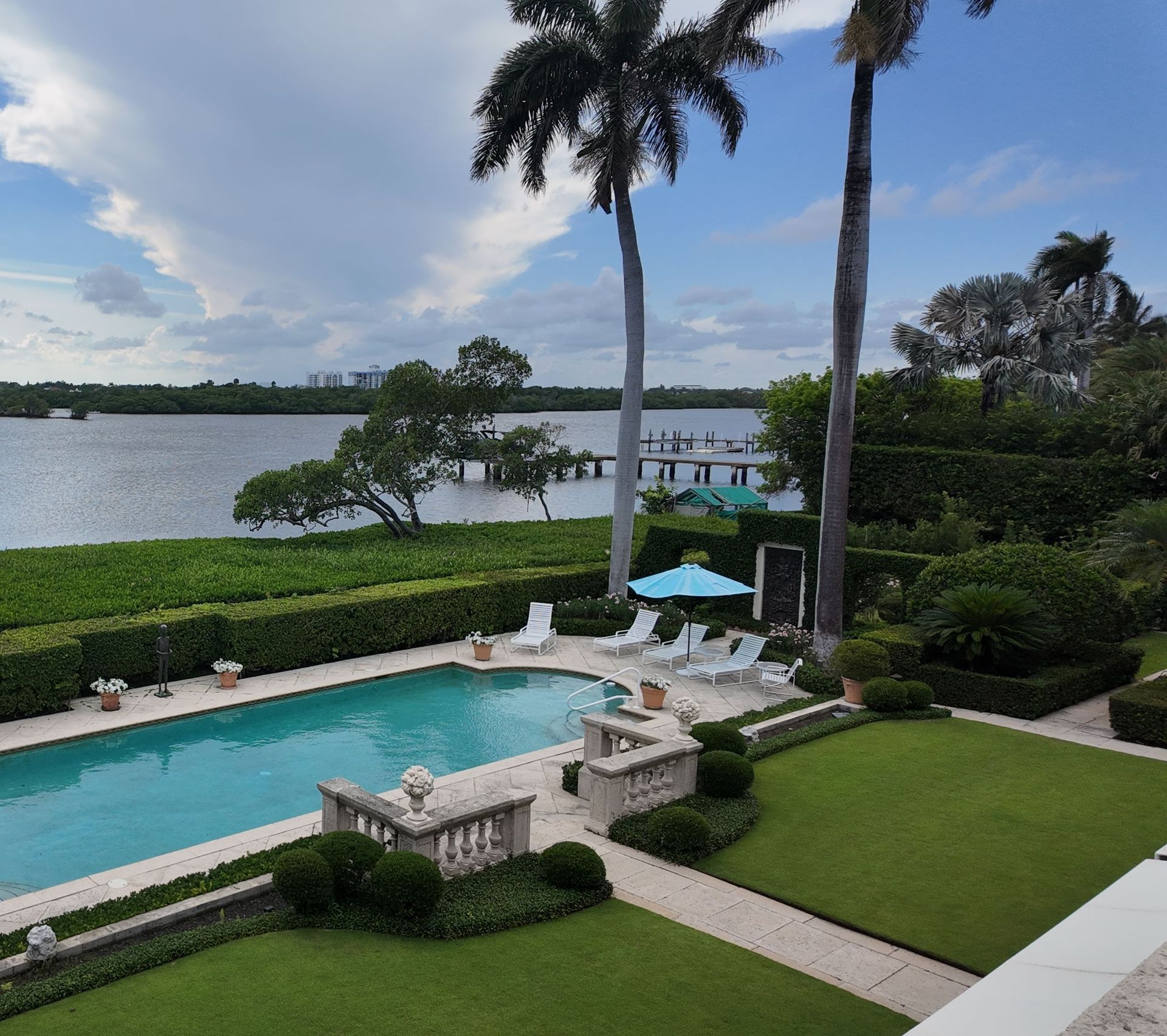 Luxury poolside patio with palm trees and a lake view under a cloudy sky