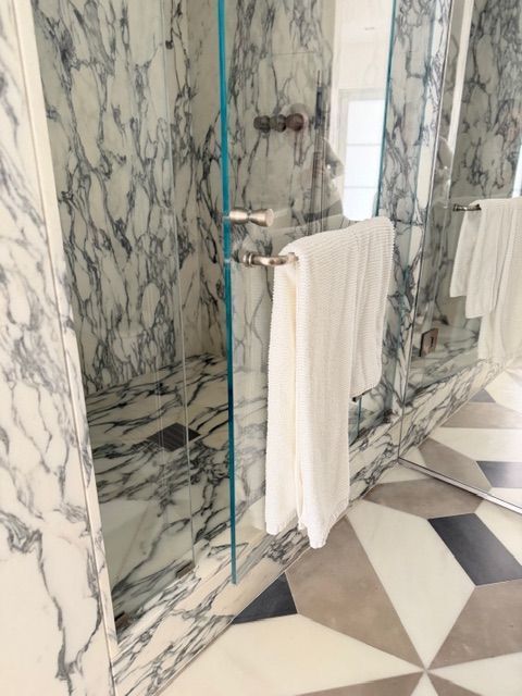 Marble-tiled bathroom with a glass shower, towel rack, and geometric floor tiles
