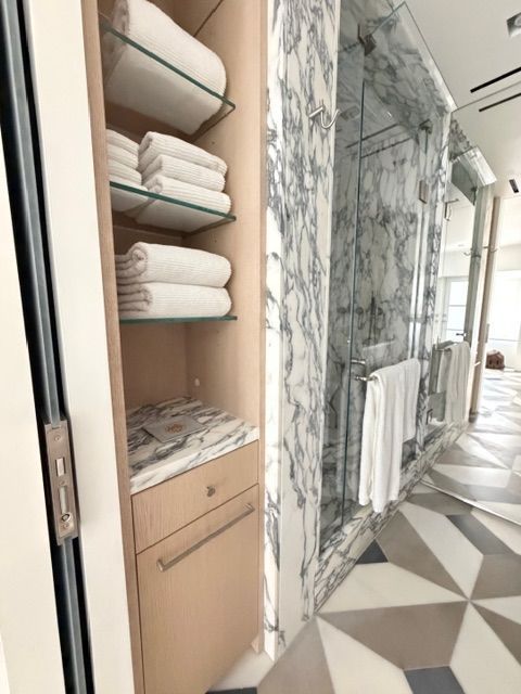 Modern bathroom with open linen shelves, marble shower, and geometric floor tiles.