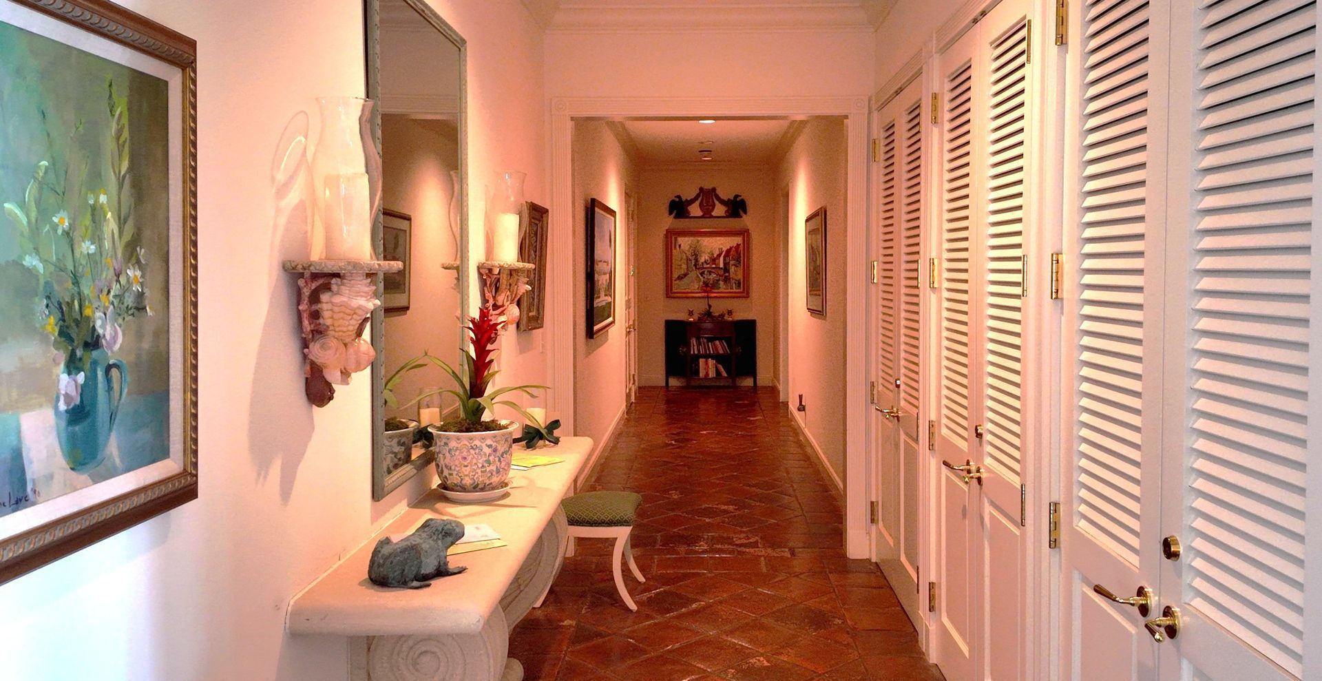 Long hallway with white louvered doors, tiled floor, and a console table with decor on the left