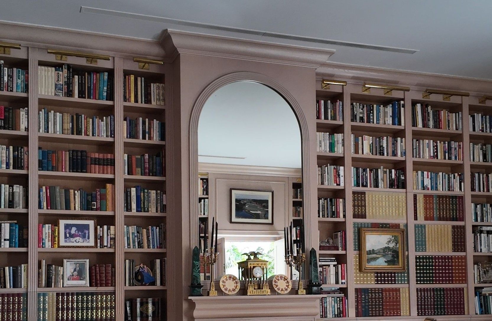 Built-in bookshelves framing a central arched mirror over a mantel in a cozy library.