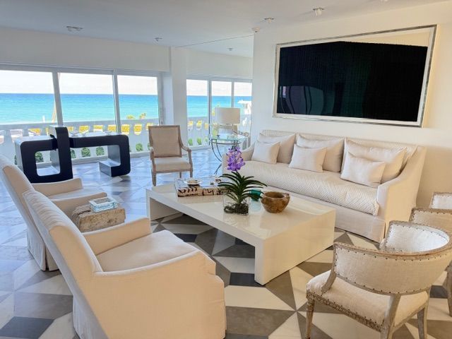 Bright coastal living room with cream sofas, white coffee table, and ocean view through large windows