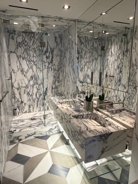 Marble-tiled bathroom with mirrored walls, glass shower, vanity, and geometric floor pattern