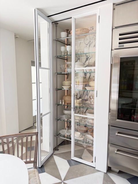 Glass display cabinet in a white kitchen, filled with dishes and decor, beside a built-in oven.