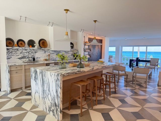 Bright modern kitchen with marble island, wood stools, geometric floor, and ocean-view dining area