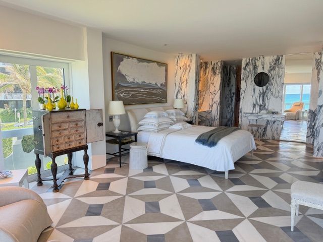 Bright bedroom with white bed, patterned floor, bay window, dresser, and coastal decor