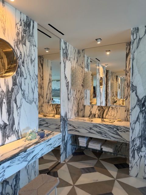 Marble-tiled bathroom with mirrors, warm lighting, and a geometric floor pattern