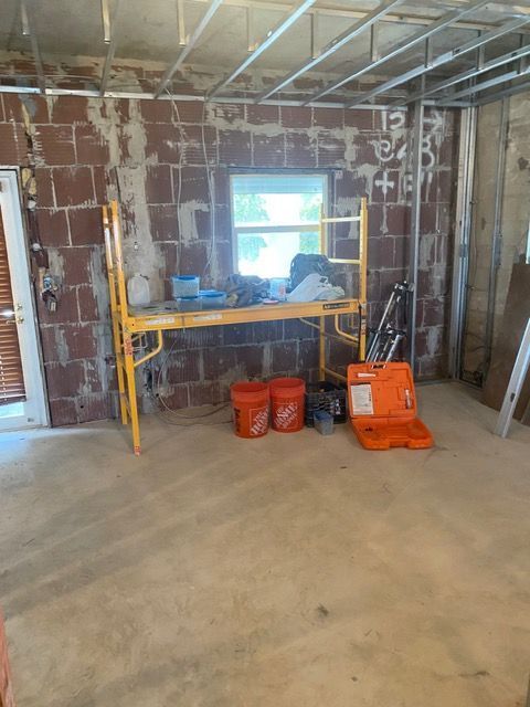Unfinished room with drywall, scaffolding, tools, and buckets during renovation.