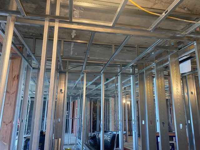 Exposed metal framing and ductwork inside an unfinished building interior, with blue sky visible through openings