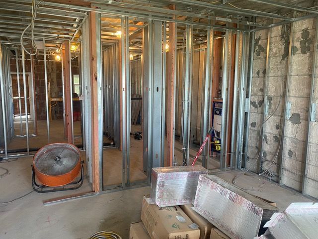 Unfinished room under construction with exposed studs, wiring, insulation, and a large orange fan.