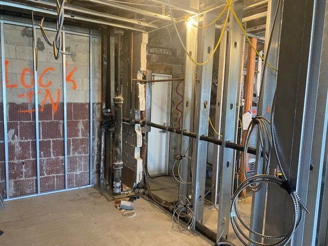 Unfinished basement wall with exposed studs, insulation, electrical wires, and coiled cable on the right
