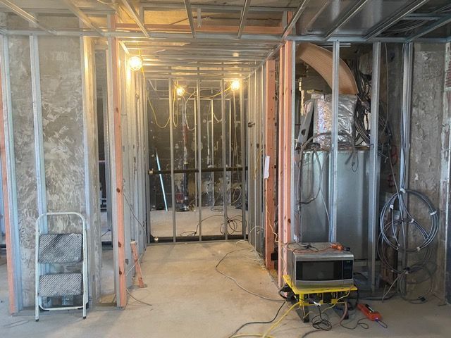 Unfinished basement framing with exposed studs, insulation, ducts, and a small cart in the center.