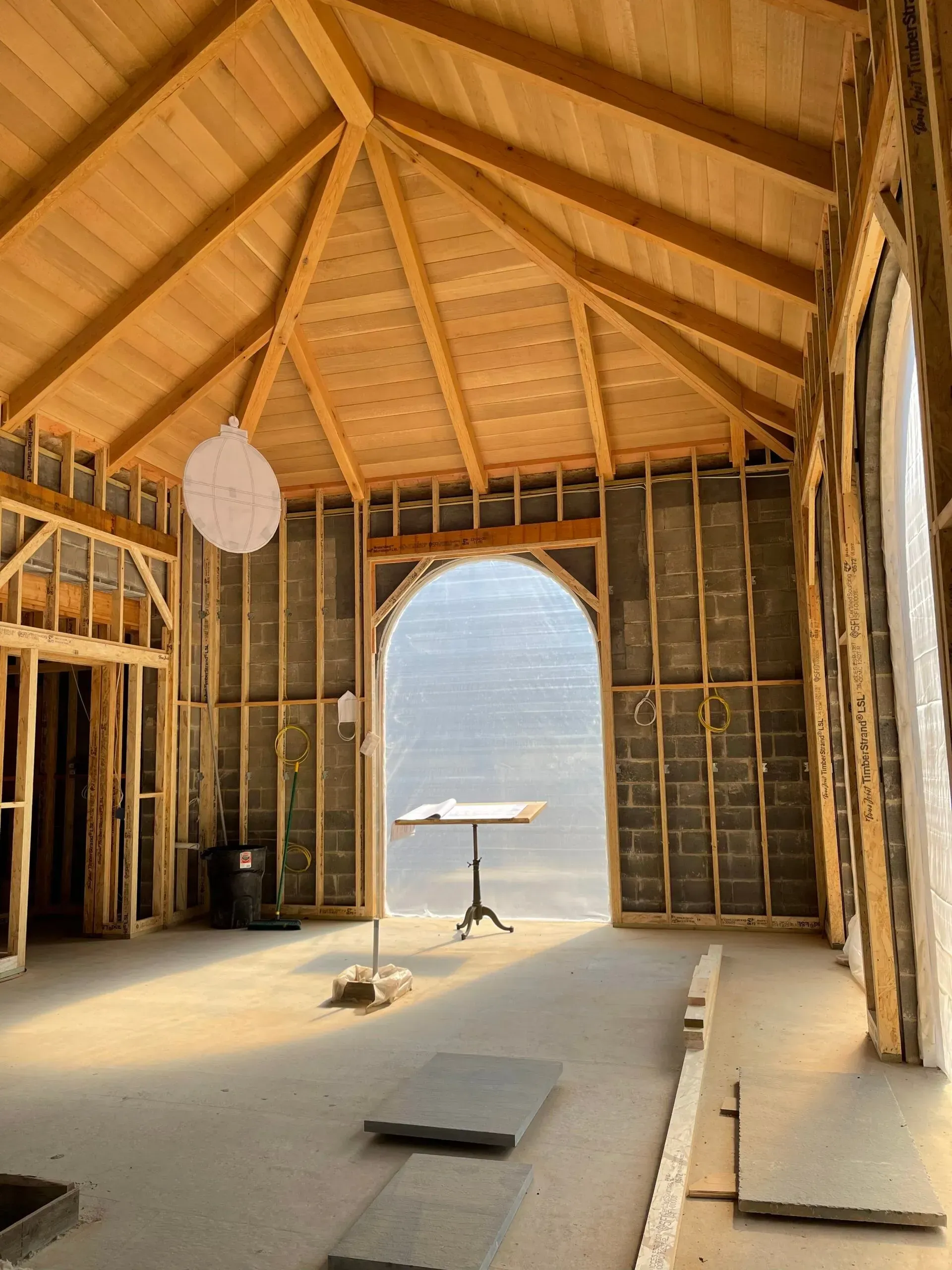Unfinished wooden interior with vaulted ceiling, exposed framing, and bright arched doorway to the outside
