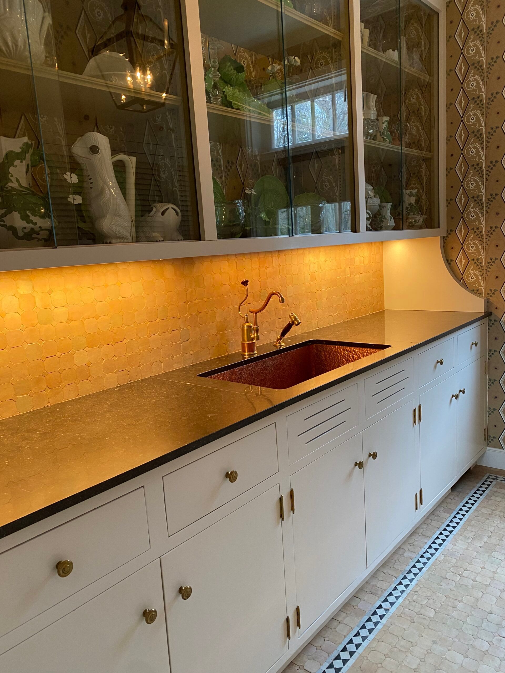 A kitchen with a sink , cabinets , and glass shelves.