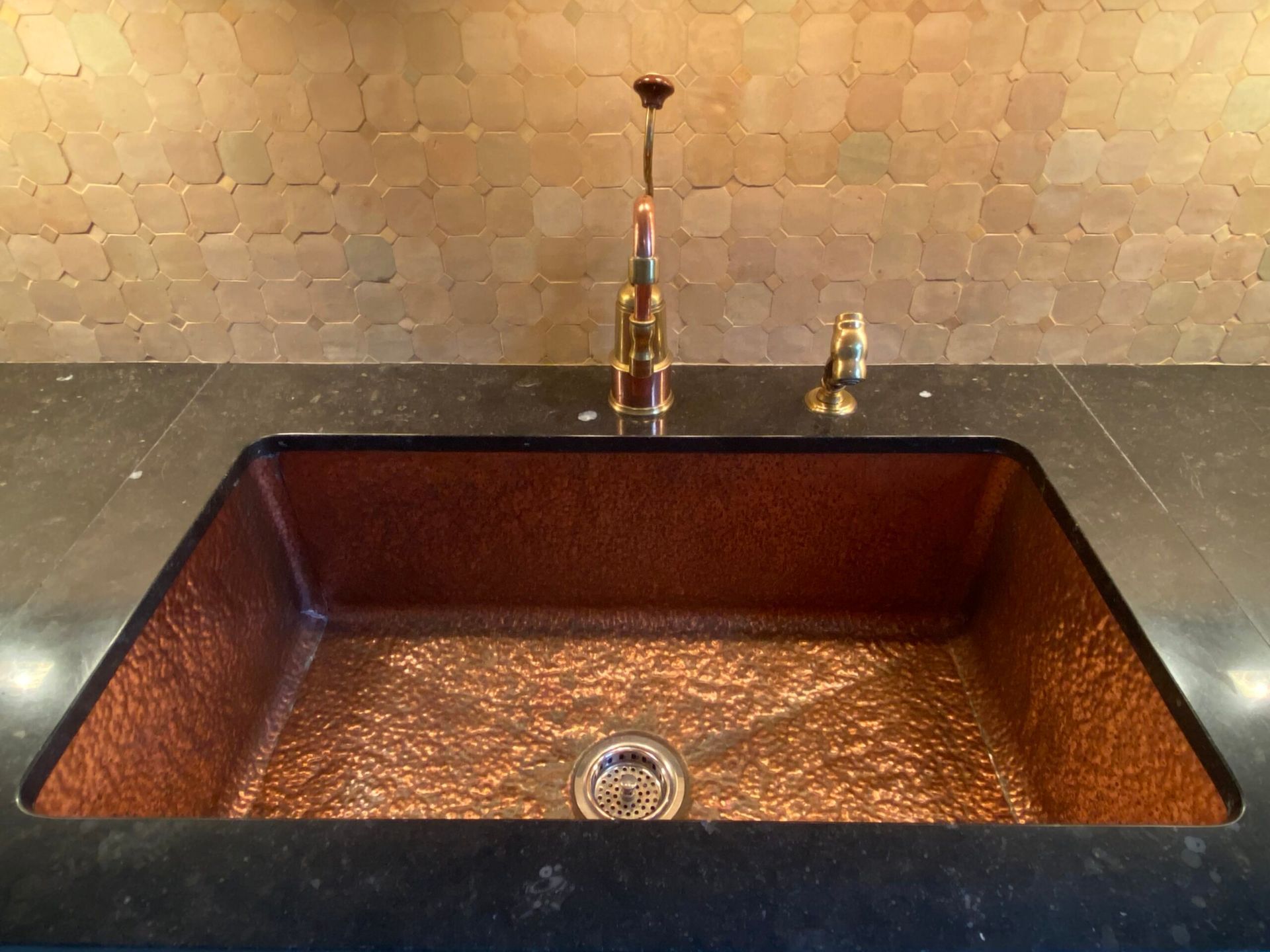 A copper sink with a black counter top