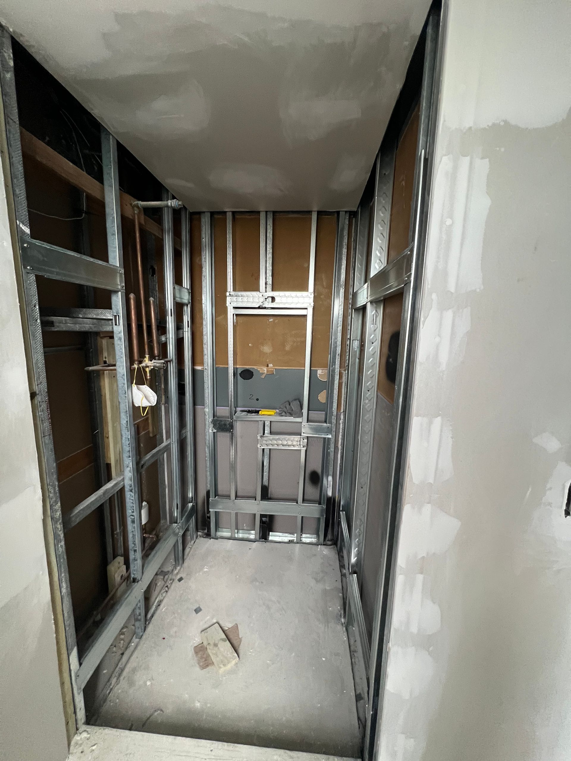 Narrow unfinished hallway with exposed studs, drywall seams, and a ladder at the far end