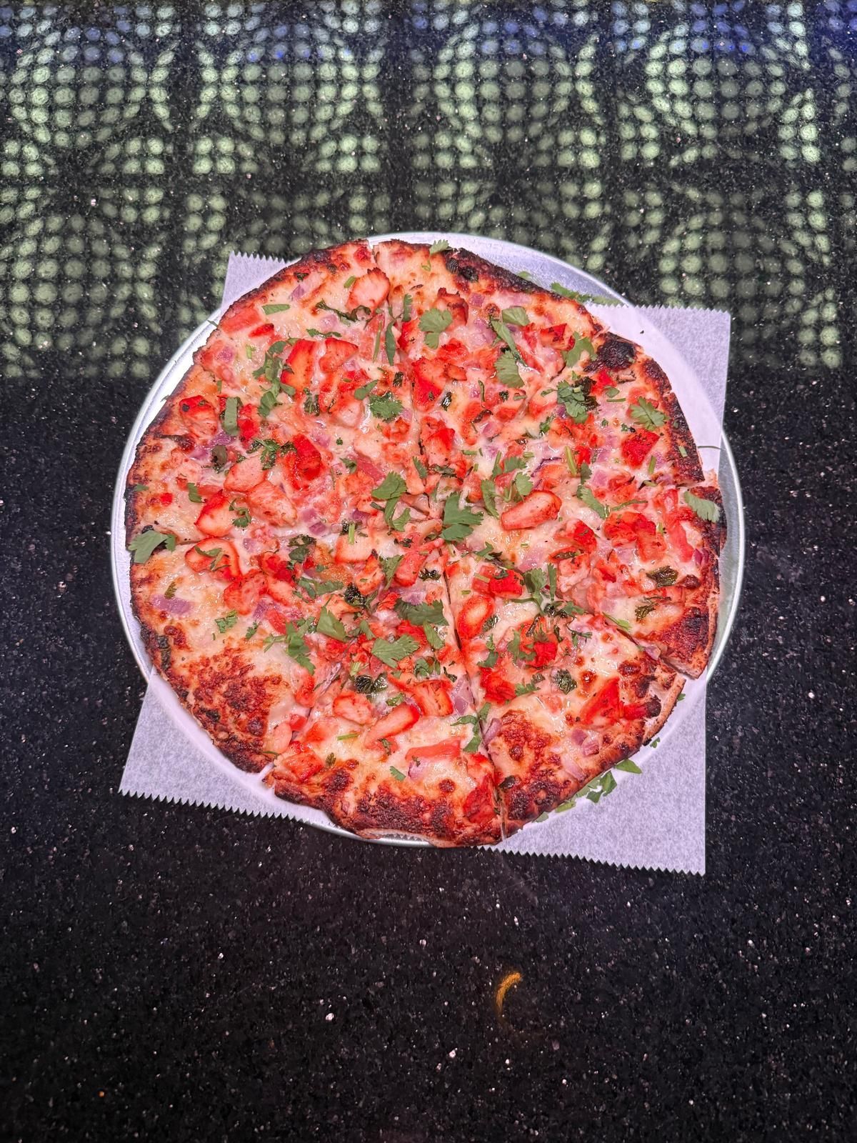A circular pizza topped with red tomato sauce, melted cheese, and fresh green herbs on a square paper liner.