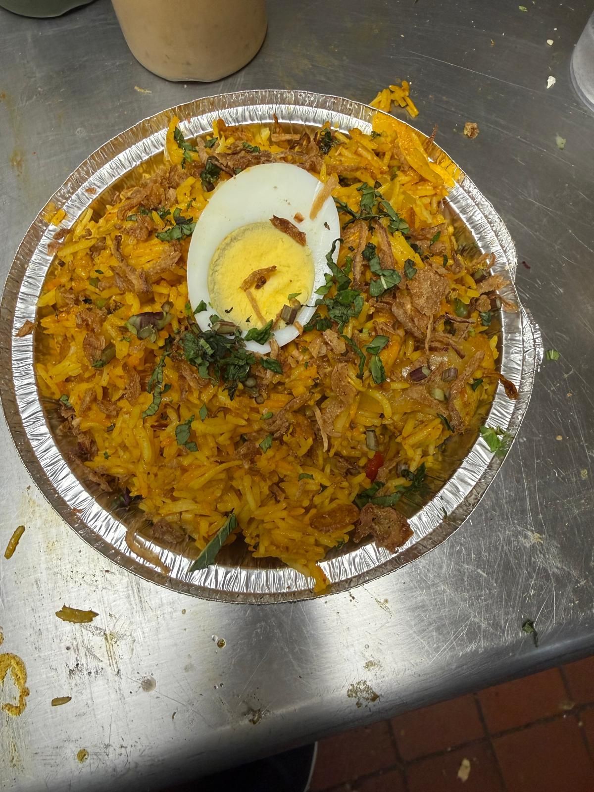 A top-down view of a container of yellow rice topped with a sliced hard-boiled egg and fresh green herbs.