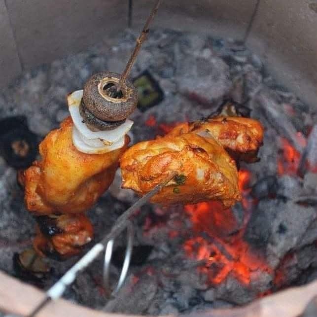 Skewered pieces of marinated chicken, mushroom, and onion cooking over glowing charcoal embers in a tandoor oven.