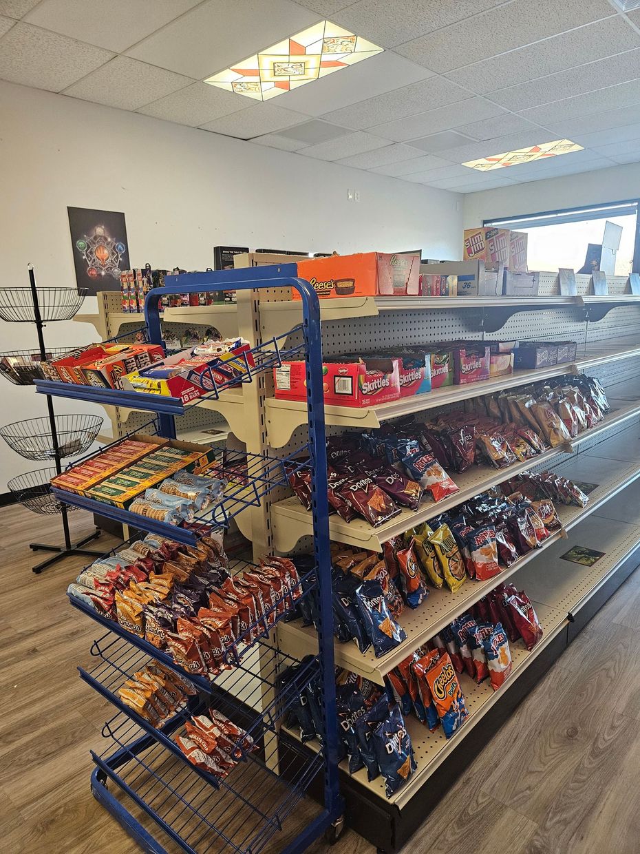 Convenience store snack aisle with blue and black display racks, chips, candy, and a bright ceiling.