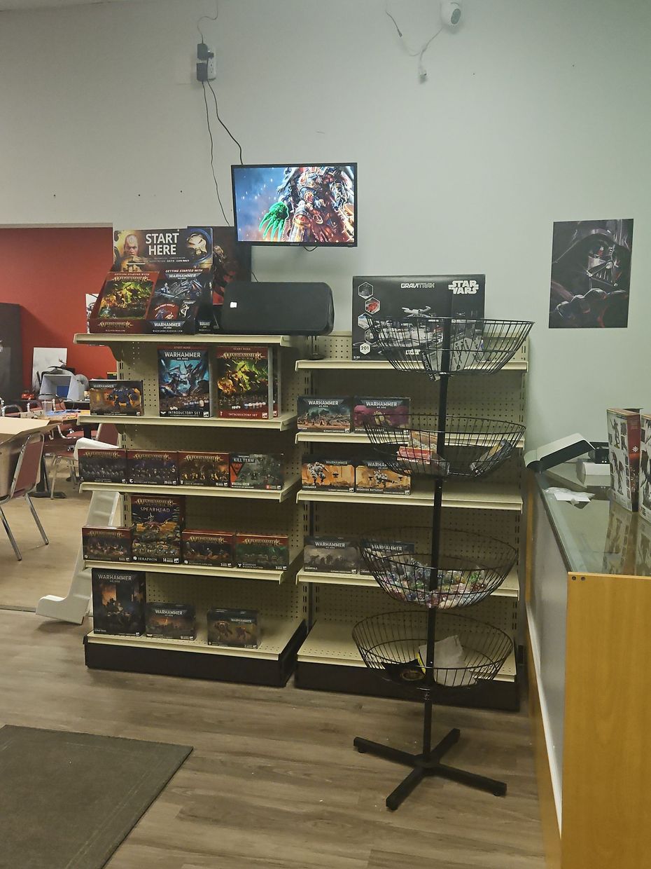Retail display shelves with colorful items, a TV screen above, and a black stand in a small shop.