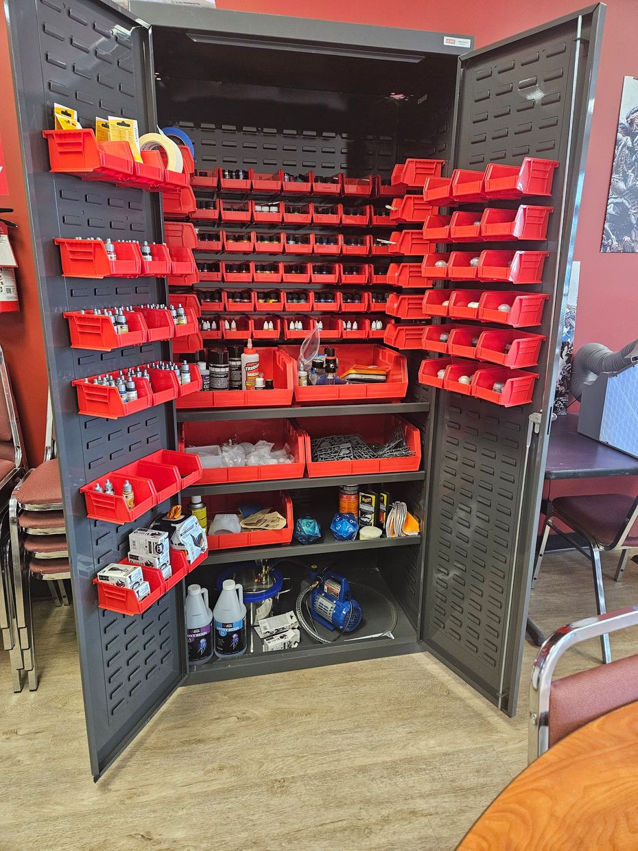 Open storage cabinet with rows of red plastic parts bins and tools in a workshop