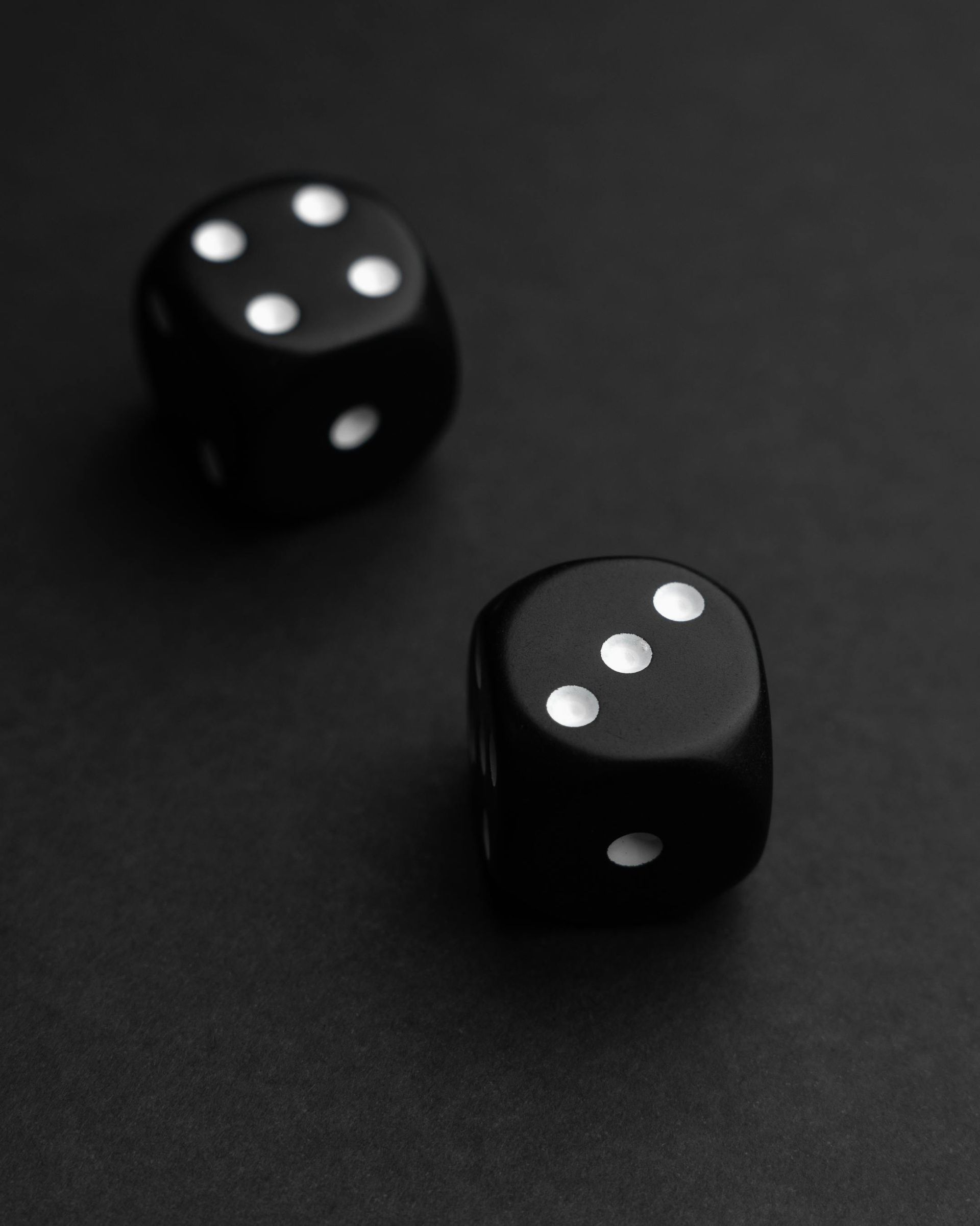 Two black dice on a dark surface, each showing different white pips.