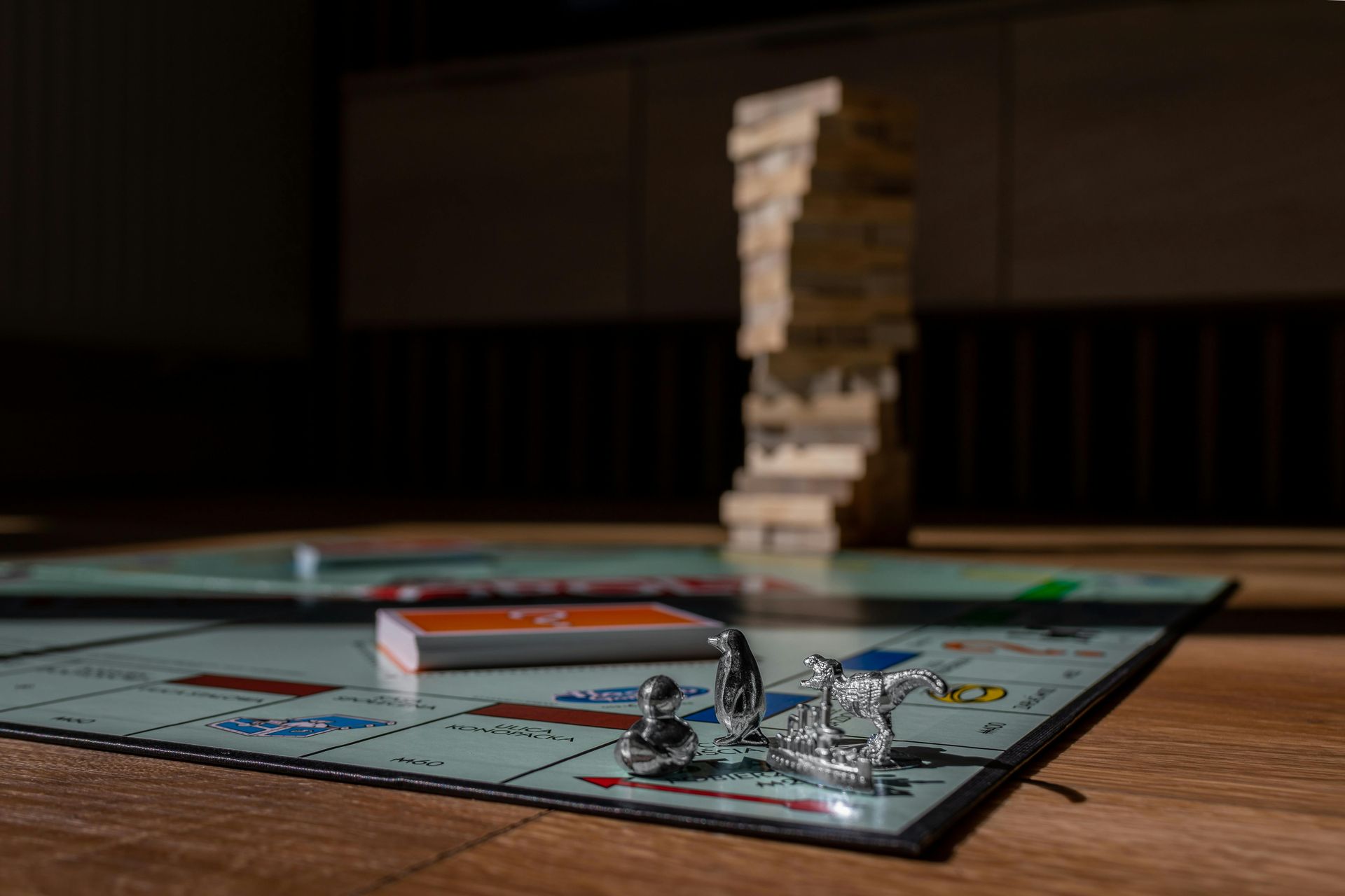 Monopoly board with pieces in the foreground and a Jenga tower in the background on a wooden table
