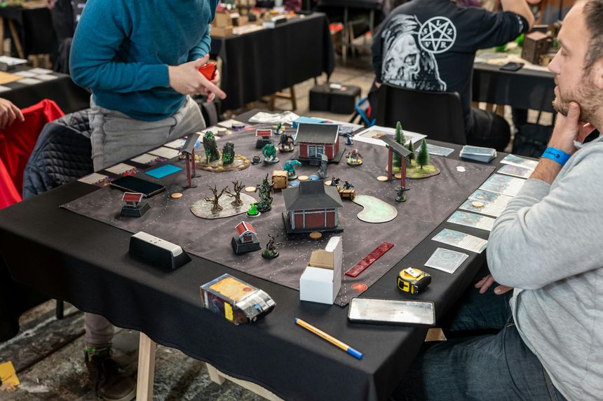 People playing a tabletop strategy game on a black table with miniatures, cards, and dice.
