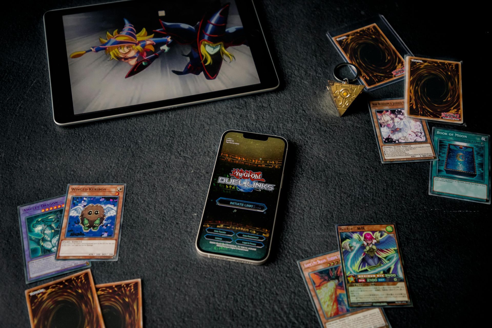 Yu-Gi-Oh! cards and a smartphone on a dark tabletop, with cards scattered around a digital duel interface