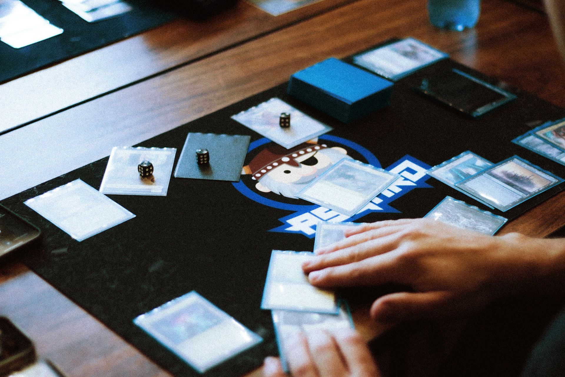 Hands arranging cards on a tabletop game board with blue and white pieces.