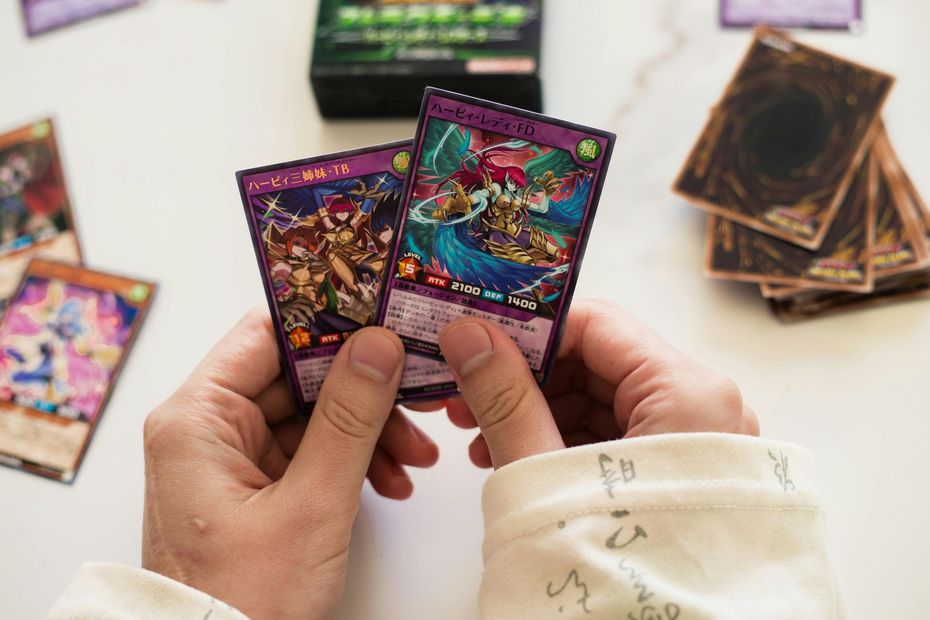 Hands holding two colorful trading cards over a tabletop with more cards and a deck in the background