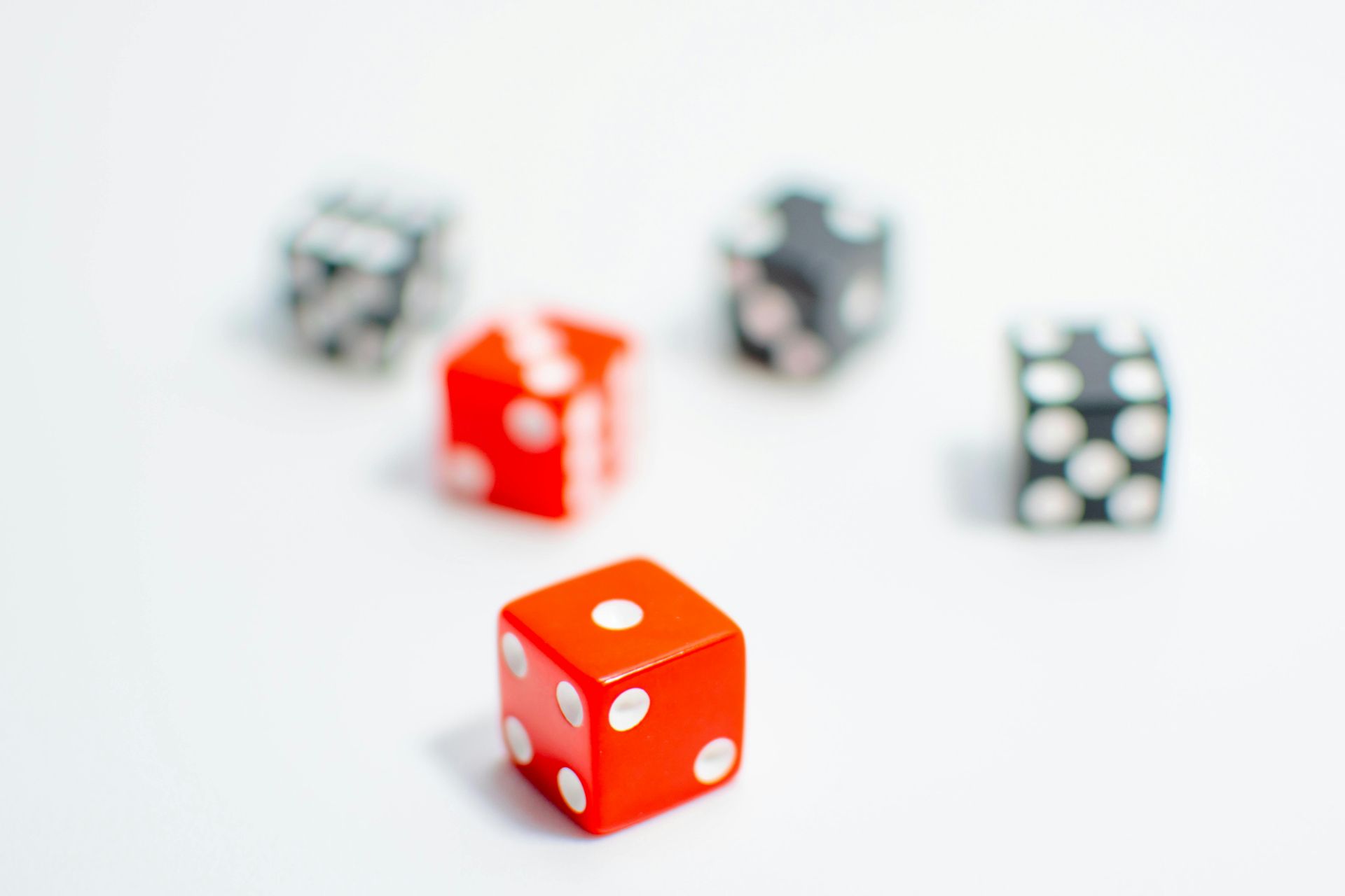 Five dice on a white surface, with a red die in focus and blurred dice behind it