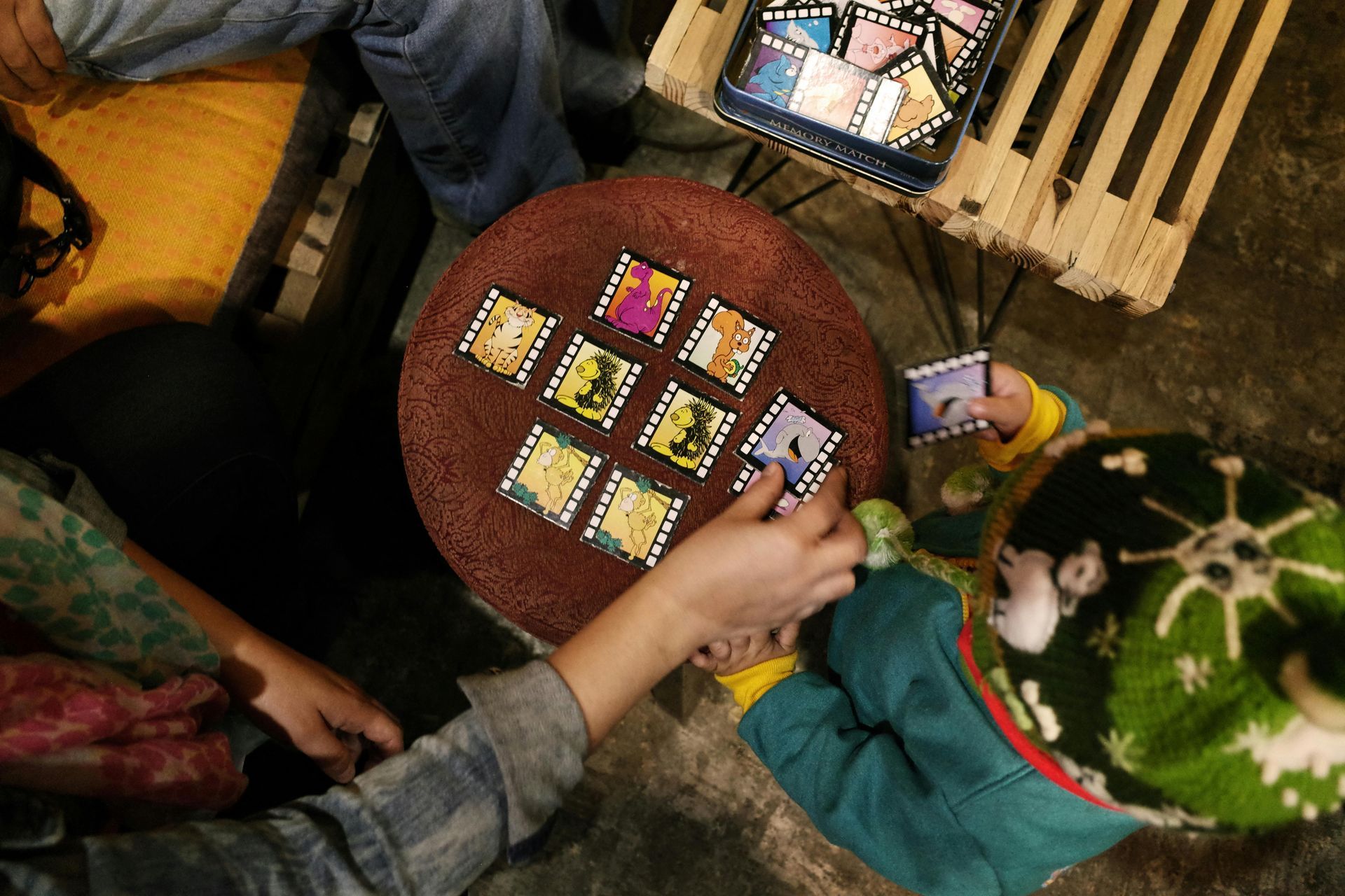 Hands arranging colorful cards on a round table beside a green patterned box and wooden slats.