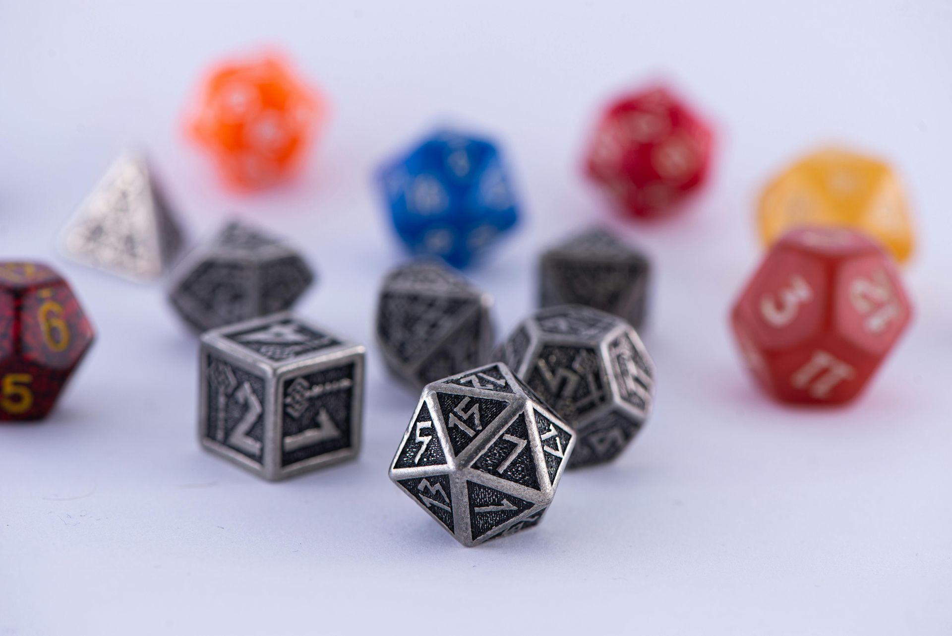 Assorted colorful polyhedral dice scattered on a white surface, with black dice in focus upfront