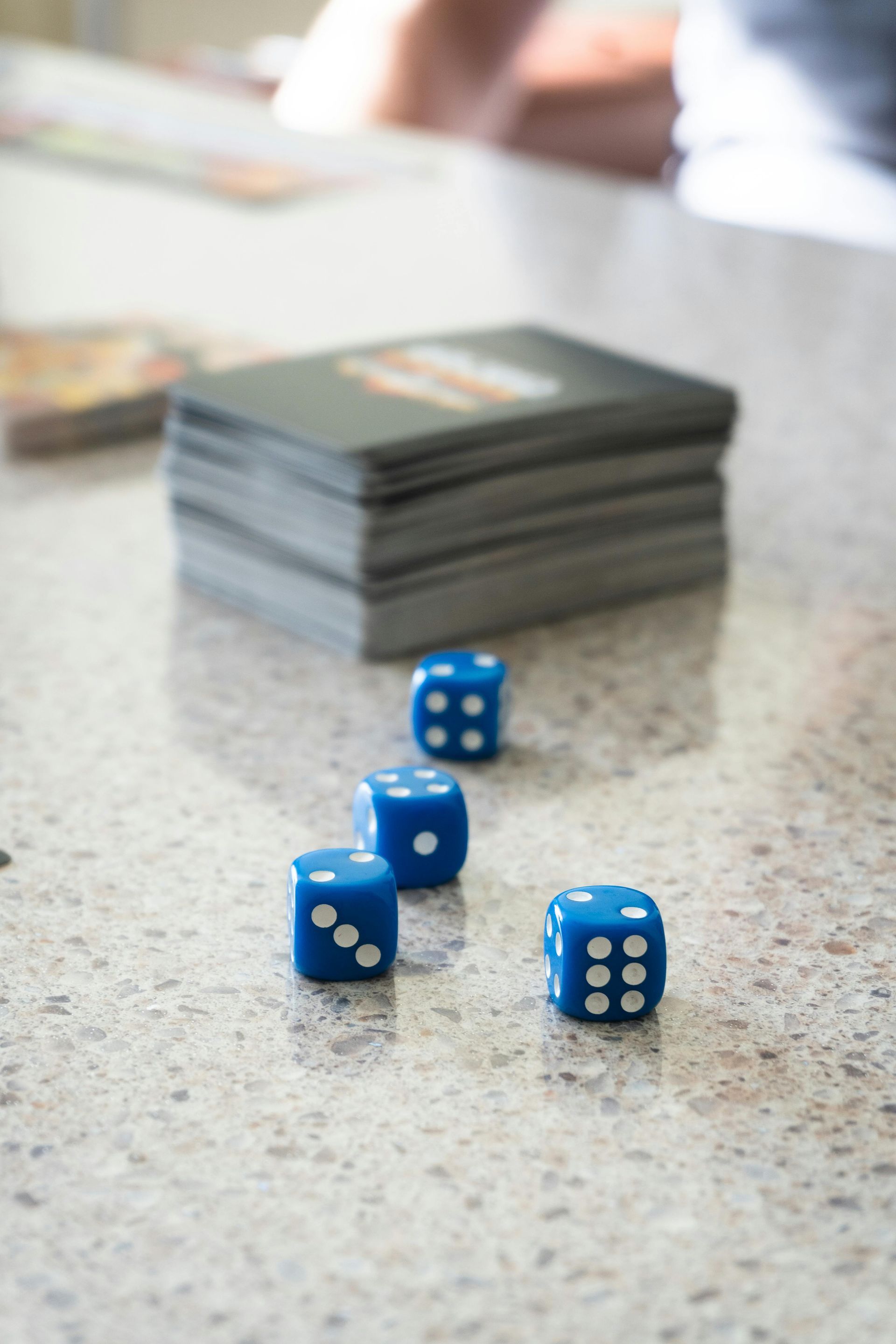 Blue dice on a speckled table beside a stacked deck of cards