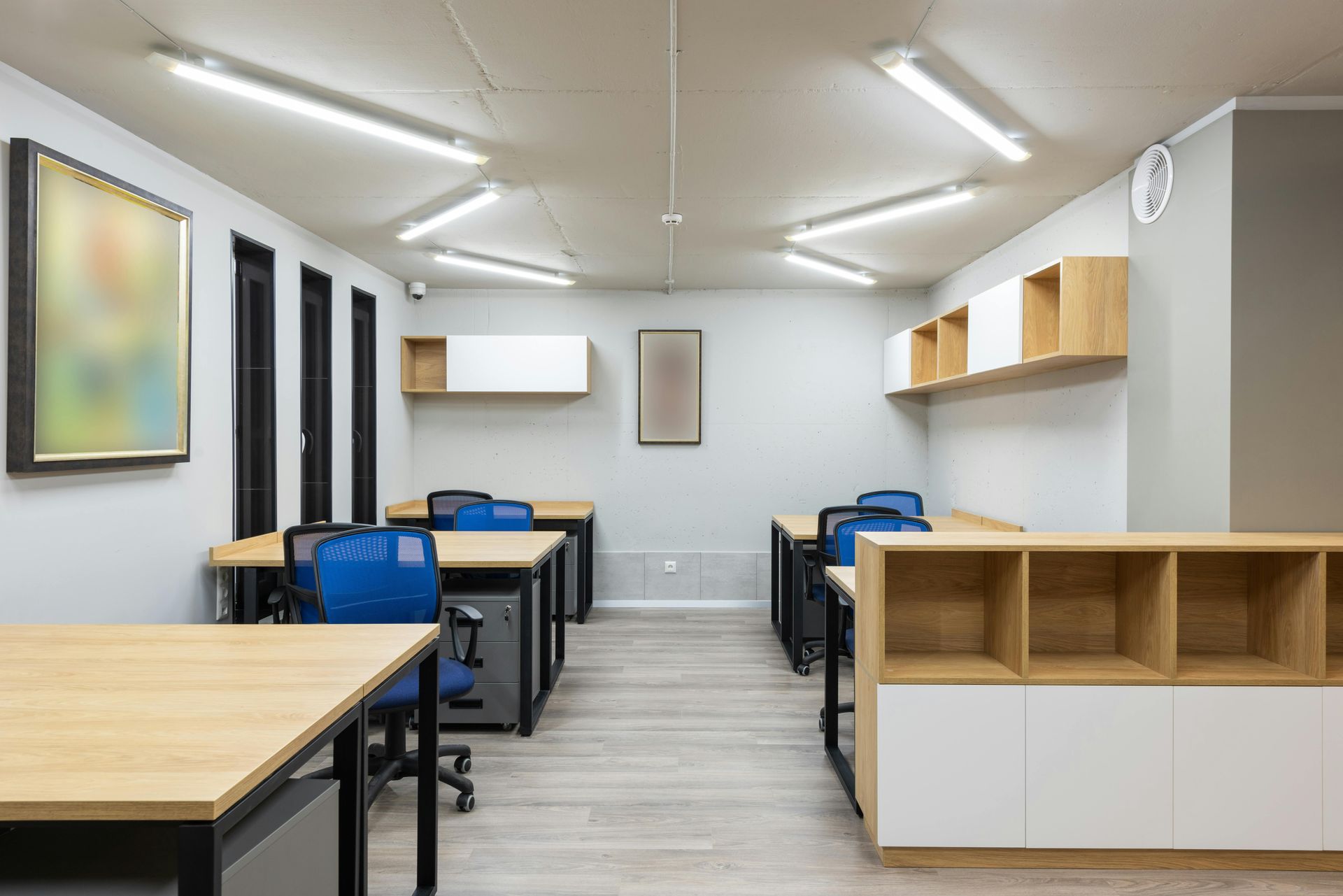 Empty modern classroom with tables, blue chairs, white walls, and overhead fluorescent lights