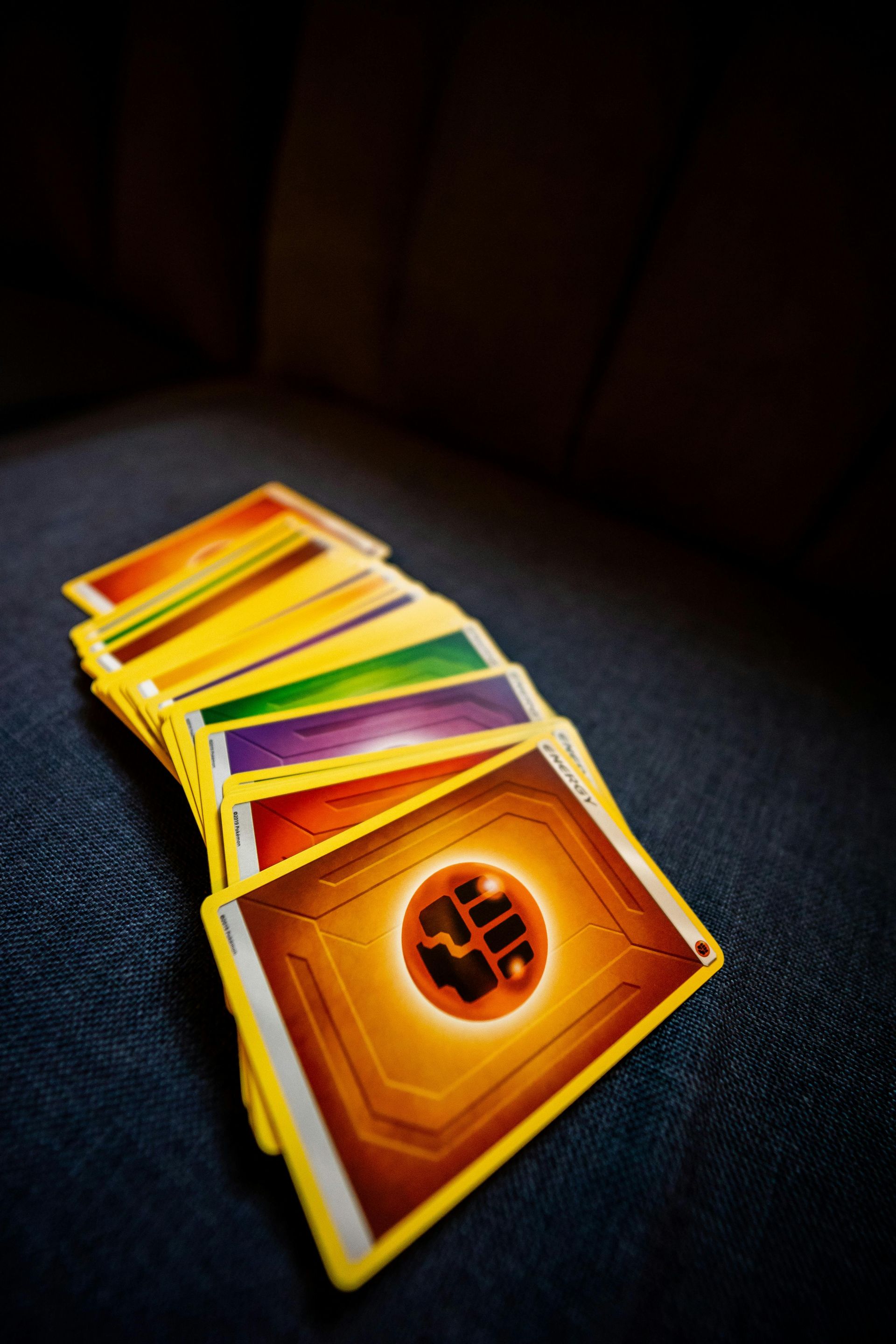 A fan of colorful trading cards on a dark surface, with a fiery orange card in front