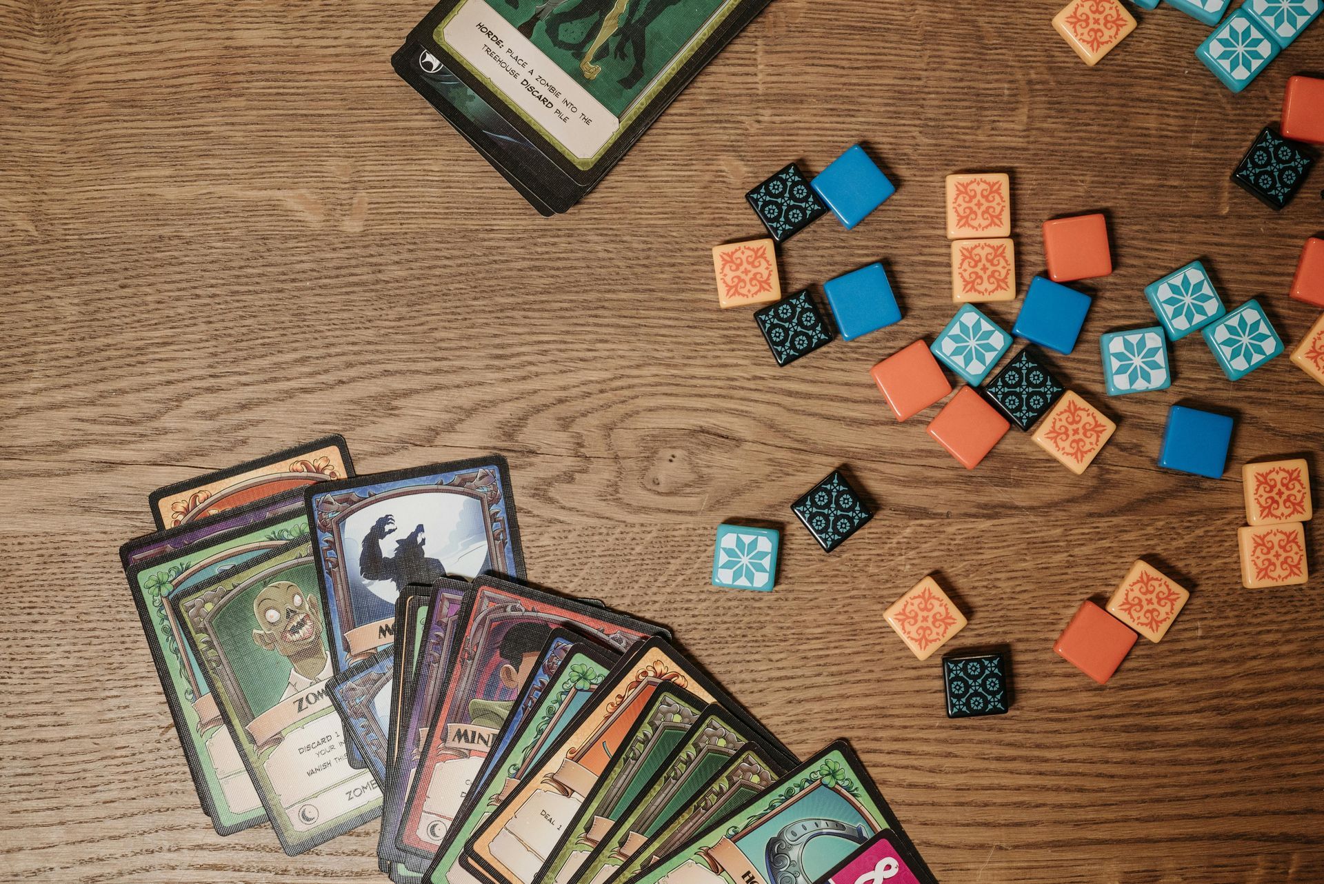 Board game cards and colored cubes scattered on a wooden table, with cards fanned at the bottom.